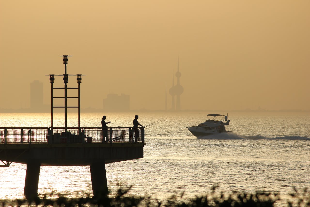 Fishermen silhouetted against a sunset, Kuwait Towers in the background.