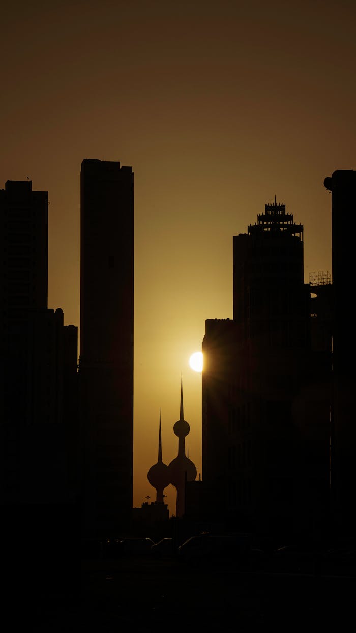 Silhouette of Kuwait City's skyline with a vibrant sunset backdrop, highlighting the urban landscape.